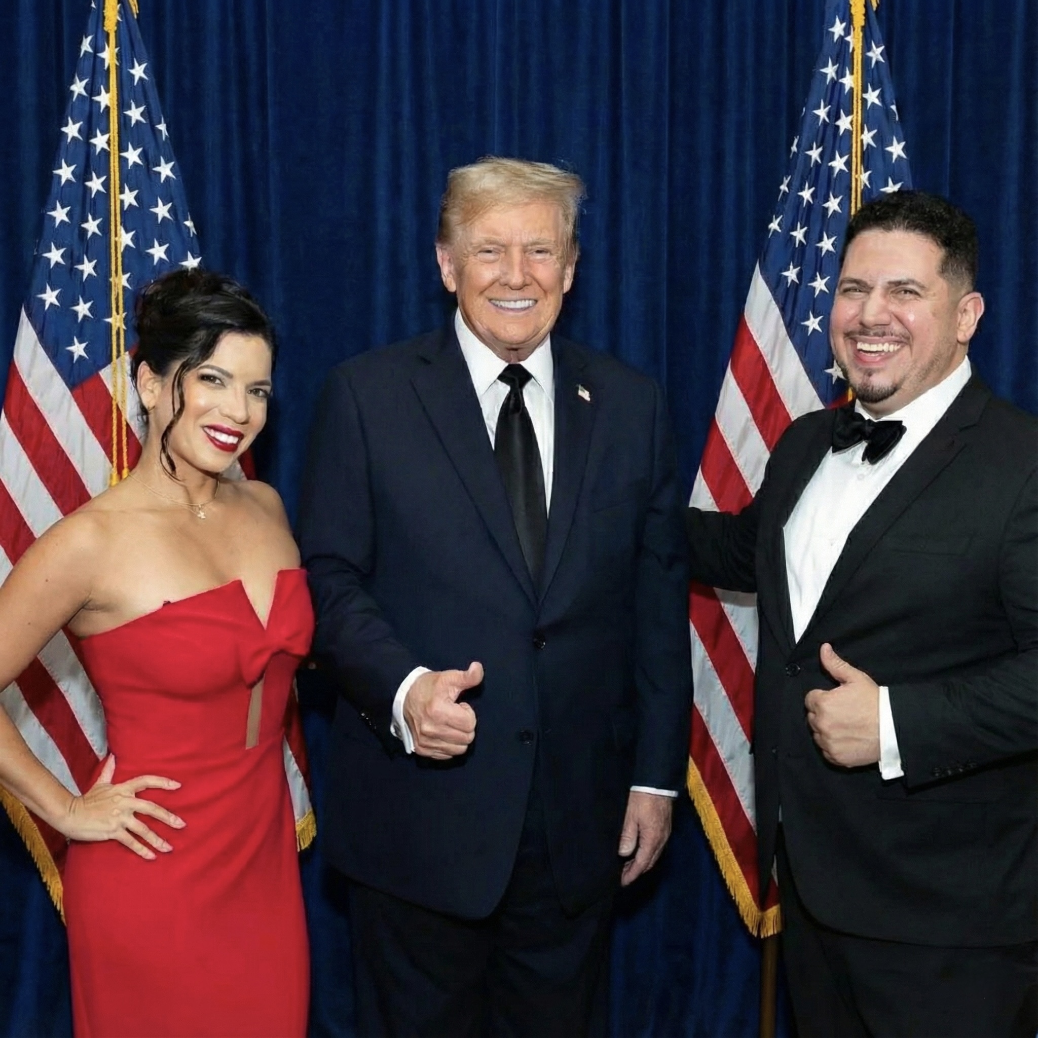 Three people in formal attire standing in front of American flags.